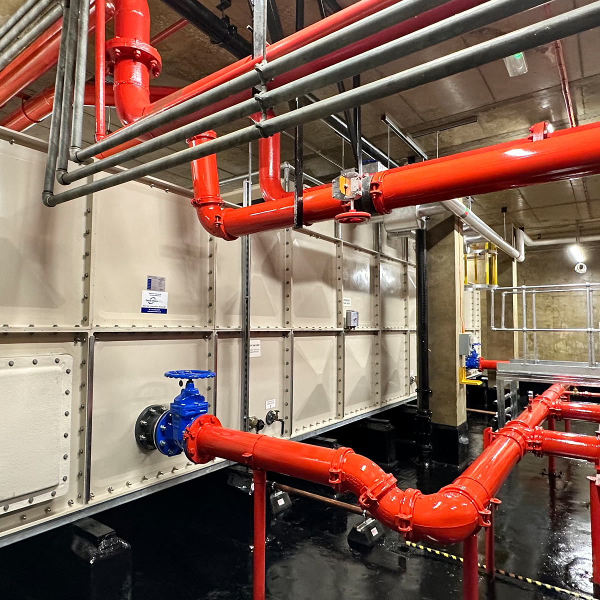 Red fire sprinkler riser pipework and gate valve at a building water storage tank